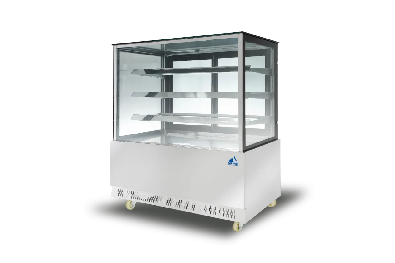 The Wide Body Commercial Cake Display Cabinet | PNR-D in a white finish, with clear glass panels on all sides and adjustable aluminum shelves. The cabinet features the SKADI logo and is equipped with wheels for mobility.