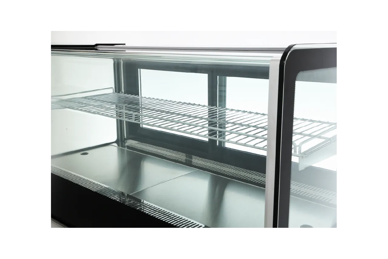 Close-up of the interior shelf inside the Spacious Countertop Cake Display Cabinet | CTR, showing a stainless steel bottom tray and a wire rack shelf. The glass panels on all sides ensure full visibility of the items displayed inside.