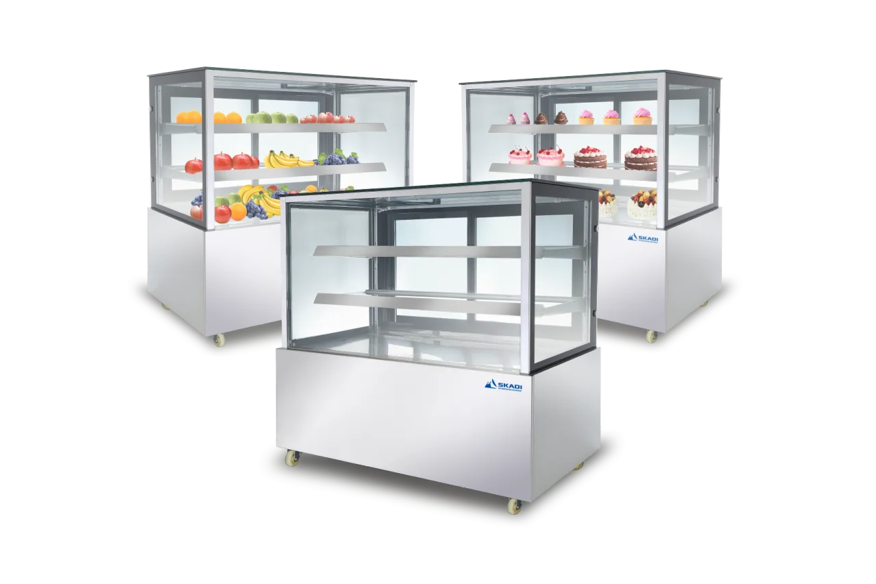 Three Skadi refrigerated display cabinets showcasing fresh produce and desserts. The units have stainless steel finishes and clear glass shelves, highlighting their use in displaying a variety of food items such as fruits and cakes in retail environments.